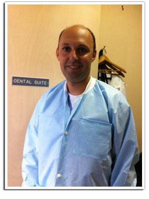 The image shows a man wearing a white lab coat standing in front of a sign that reads  Dental Suite.