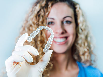 The image shows a woman holding up a transparent mouthguard with her right hand.