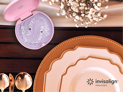 The image shows a collection of tableware items including plates, bowls, and a small, pink, decorative object with a face design, set against a background that includes a wooden table, a vase with flowers, and a bottle of toothpaste branded  Invisalign.