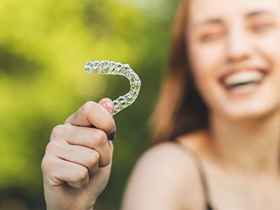 A woman holding up a clear plastic toothbrush with a smiling expression.