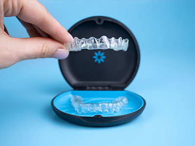 The image shows a hand holding an open box containing a set of dental braces with a blue background highlighting the product.