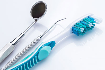 A dental care setup on a white background, featuring a toothbrush with blue bristles, a pair of scissors, and a dental mirror.