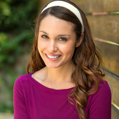 A woman with long hair smiling at the camera while standing against a wooden fence.