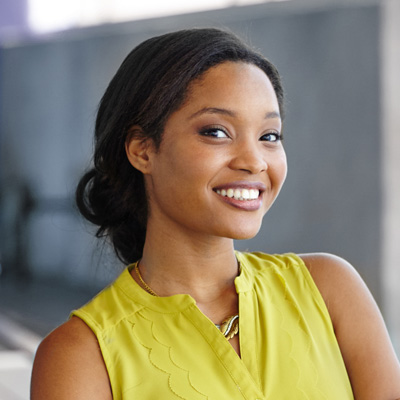 The image features a woman with a radiant smile, wearing a yellow top, posing confidently against a backdrop.