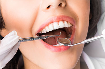 A woman wearing a white lab coat has her mouth open wide, revealing teeth, while holding dental tools, possibly during a dental procedure.