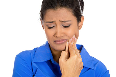 A woman with her eyes closed, holding her face and looking distressed while standing against a plain background.