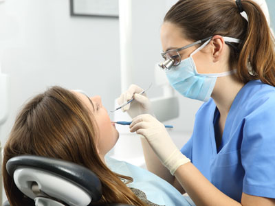 A dental hygienist in a blue uniform is performing dental work on a patient while wearing protective eyewear.