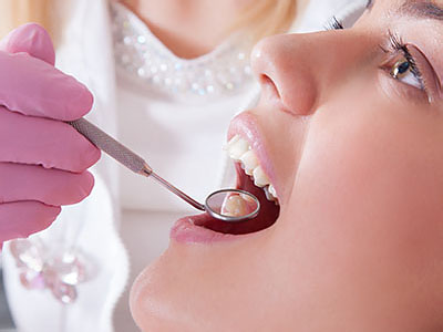 The image shows a person receiving dental treatment, with a dentist using a dental drill on their teeth while wearing protective gloves and a surgical mask.