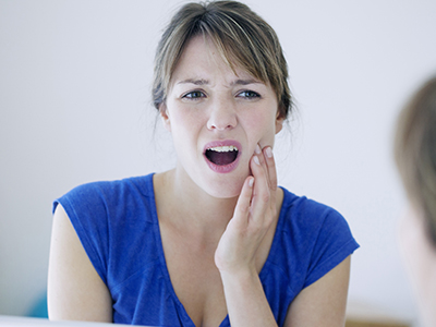 A woman with her mouth open, looking at her reflection in the mirror, showing signs of distress or concern.