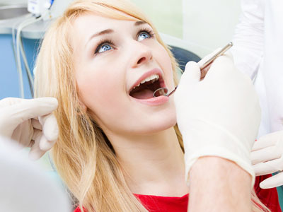 A woman in a dental chair is receiving dental treatment with an open mouth, while a dentist in protective gear works on her teeth.