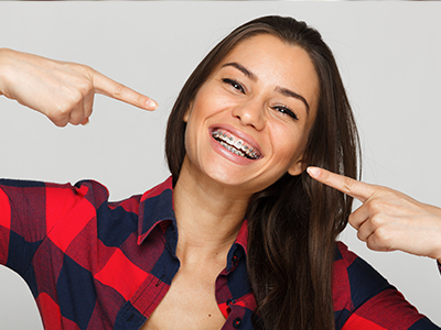 The image shows a woman with a wide smile pointing directly at the camera, highlighting her teeth, set against a white background.