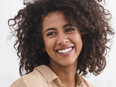 The image shows a smiling woman with curly hair wearing a light-colored top, looking directly at the camera.